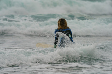 Water splashes around young surfer looking for an epic barrel wave. Extreme woman sportsman surfing a wave in Basque Autonomous Community in summer cloudy day. Lesson in the surfing school.