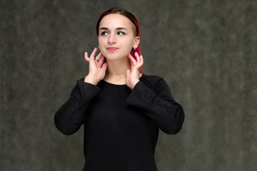 Portrait to the waist of a pretty girl with red hair on a gray background in a black jacket. Standing right in front of the camera in a studio with emotions, talking, showing hands, smiling