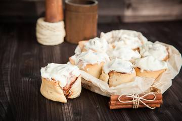 Obraz na płótnie Canvas fresh cinnamon rolls and cream on a wooden background, cinnamon sticks