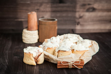 fresh cinnamon rolls and cream on a wooden background, cinnamon sticks