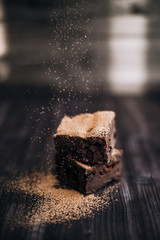 brownie cake sprinkled with ground cocoa on a dark background