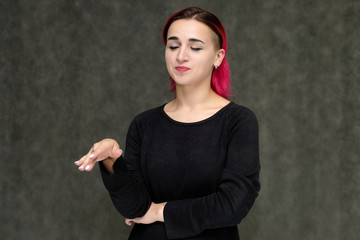 Portrait to the waist of a pretty girl with red hair on a gray background in a black jacket. Standing right in front of the camera in a studio with emotions, talking, showing hands, smiling