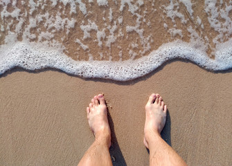 clear sea waves on sand beach in daytime with man foots vacation