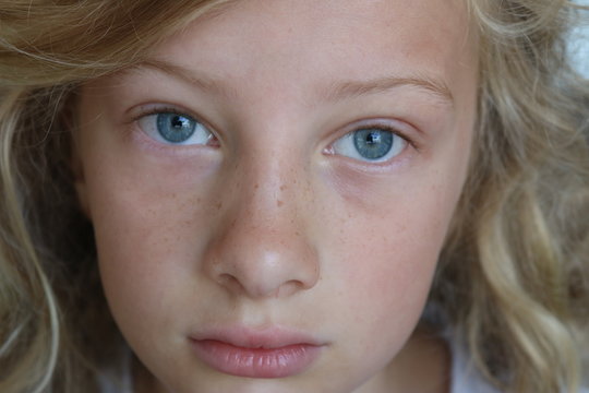 Closeup of a beautiful preteen girl with blue eyes and a sad, serious stare