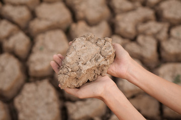 Hand holding a dry soil with cracked earth on background metaphor climate change, water crisis, environmental problems