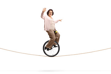 Senior woman riding a unicycle on a rope and waving © Ljupco Smokovski