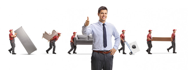 Young professional man showing thumbs up and movers carrying furniture