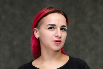 Close-up Portrait of the shoulders of a pretty girl with red hair on a gray background in a black jacket. Standing directly in front of the camera in the studio with emotions, talking, smiling.