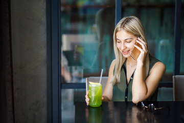 A young beautiful blonde girl sits in a cozy cafe, talks on the phone and drinks a cooling drink. Rest in the summer heat