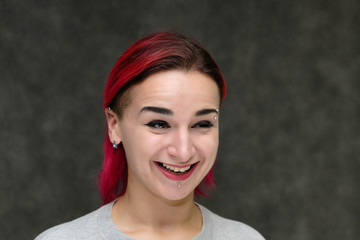 Close-up portrait on the shoulders of a pretty girl with red hair on a gray background in a gray jacket. Standing directly in front of the camera in the studio with emotions, talking, smiling.