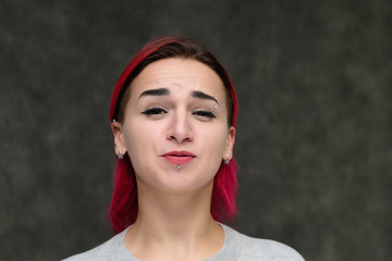 Close-up portrait on the shoulders of a pretty girl with red hair on a gray background in a gray jacket. Standing directly in front of the camera in the studio with emotions, talking, smiling.