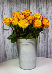 yellow roses in a metal vase on a wooden wall background