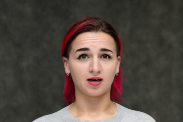 Close-up portrait on the shoulders of a pretty girl with red hair on a gray background in a gray jacket. Standing directly in front of the camera in the studio with emotions, talking, smiling.