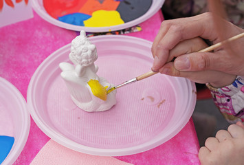 Child paints a ceramic figurine with bright colors. Ceramic staruette for coloring.