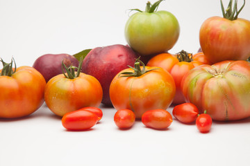 Fototapeta na wymiar Nectarinas, tomates maduros y tomates cherri sobre un fondo blanco. Los productos han sido traidos de un huerto ecológico, cultivados sin productos químicos ni pesticidas.
