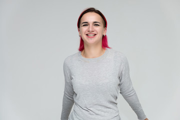 Portrait to the waist of a pretty girl with red hair on a white background in a gray sweater. Standing right in front of the camera in a studio with emotions, talking, showing hands, smiling