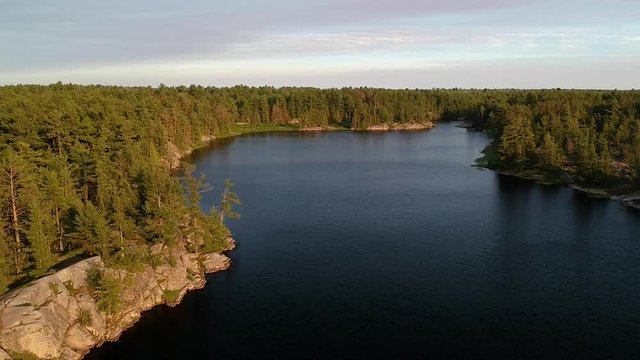 Aerial shot flying forward at high altitude above northern lake and endless boreal pine trees coniferous forest going over horizon. Shot at high angle.  Grundy lake, Northern Ontario, Canada.