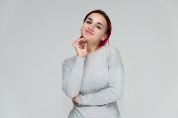 Portrait to the waist of a pretty girl with red hair on a white background in a gray sweater. Standing right in front of the camera in a studio with emotions, talking, showing hands, smiling