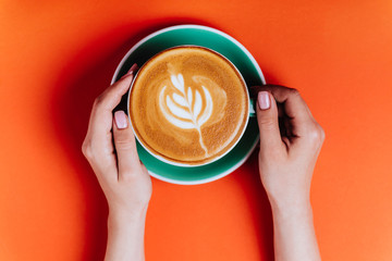 Female hands with a coffee cappuccino cyan cup. Sunny orange toned photo. Warm concept