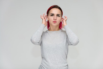 Portrait to the waist of a pretty girl with red hair on a white background in a gray sweater. Standing right in front of the camera in a studio with emotions, talking, showing hands, smiling