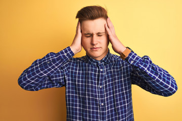 Young handsome man wearing casual shirt standing over isolated yellow background with hand on head for pain in head because stress. Suffering migraine.