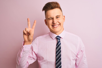 Young handsome businessman wearing shirt and tie standing over isolated pink background smiling with happy face winking at the camera doing victory sign with fingers. Number two.