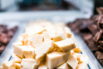 Macro closeup of pile of many white chocolate pieces chunks on tray glass display in candy store dessert chocolatier shop