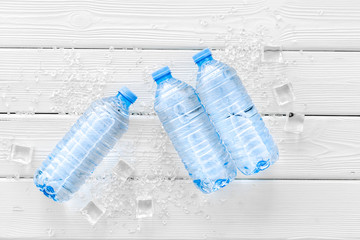 empty plastic bottles for pure water with ice cubes on white wooden background top view