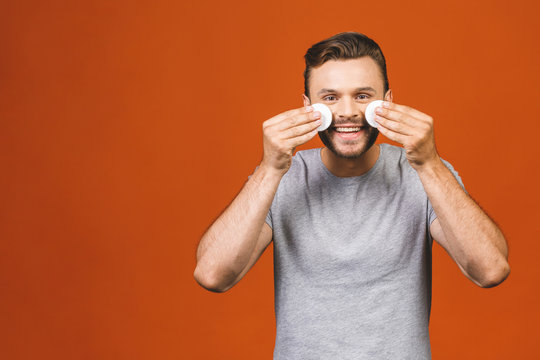 Beauty portrait of half naked confident young man using cotton pad on his face isolated over orange background.