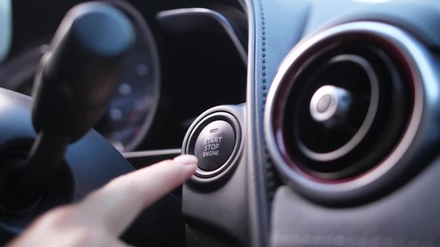 Close-up of female driver hand pressing start engine button in modern car before driving. Woman going to drive automobile and starting engine using stop/start button on dashboard, car interior view