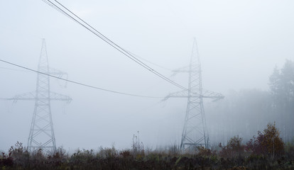 High-voltage electric towers in the fog against the background of the forest.