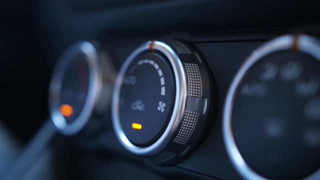 Closeup of female hand fixing car air conditioner while driving. Woman driver turning air conditioning adjustment knob on dashboard of modern automobile, interior view