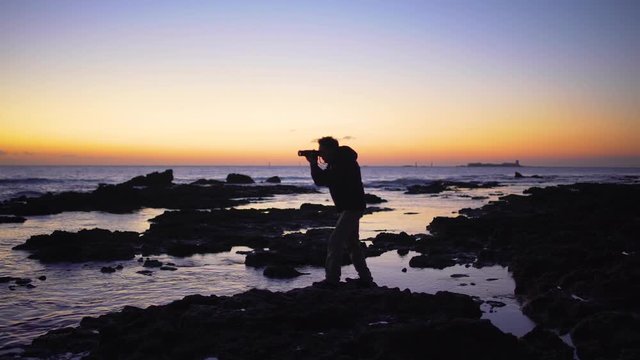 A photographer silhouette taking photos in the sea at sunset	