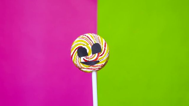 A Lollipop with the image of an aggressive face rotating against a bright background. The concept of the impact of sugar on human health.