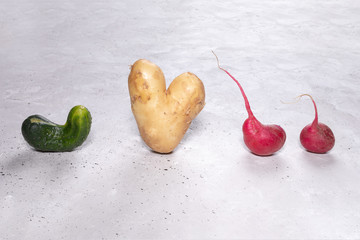Four ugly vegetables: potato, cucumber and radish on grey concrete background.