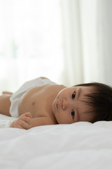 Obraz na płótnie Canvas Cute Sweet Adorable Asian Baby wearing white dress lying on white bed smiling and playing with happiness emotional in cozy bedroom,Healthy Baby Concept