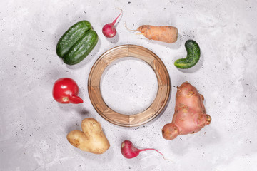 Set of ripe ugly vegetables laid around of rounded wooden frame on grey concrete background.