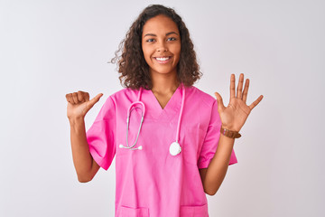 Young brazilian nurse woman wearing stethoscope standing over isolated white background showing and pointing up with fingers number six while smiling confident and happy.