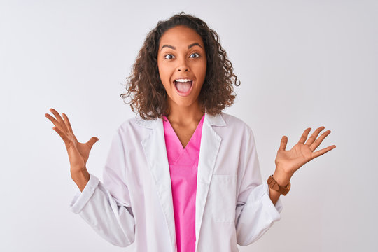 Young brazilian doctor woman wearing coat standing over isolated white background celebrating crazy and amazed for success with arms raised and open eyes screaming excited. Winner concept