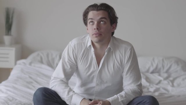 Depressed young man alone at home or hotel room. The guy falling on his bed, he is sad, tired and exhausted. Mental injury, disorder, bad mood. Front view