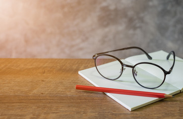 Blank open book with red pencil and glasses  on the wooden table. cement wall background, copy space.