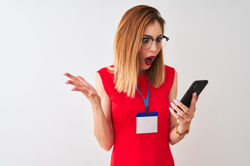 Naklejka premium Redhead businesswoman wearing id card using smartphone over isolated white background very happy and excited, winner expression celebrating victory screaming with big smile and raised hands