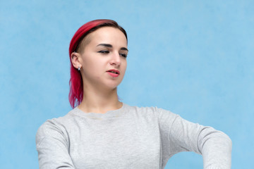 Portrait of the chest of a pretty girl with red hair on a blue background in a gray jacket. Standing in the studio right in front of the camera with emotions, talking, showing hands, smiling