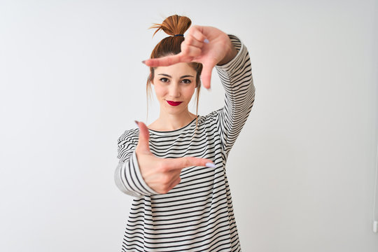 Redhead woman wearing navy striped t-shirt standing over isolated white background smiling making frame with hands and fingers with happy face. Creativity and photography concept.