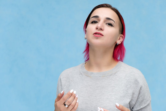Portrait of the chest of a pretty girl with red hair on a blue background in a gray jacket. Standing in the studio right in front of the camera with emotions, talking, showing hands, smiling