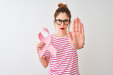 Beautiful redhead woman wearing glasses holding cancer ribbon over isolated white background with open hand doing stop sign with serious and confident expression, defense gesture