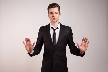  A married man with a ring on his finger expresses protest with his hands. In a black suit on a white background. Do not come, do not touch, I have problems.