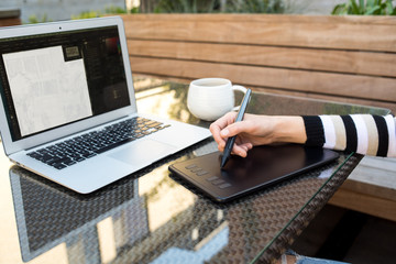 Detail photo of woman using drawing tablet and laptop on outdoor patio