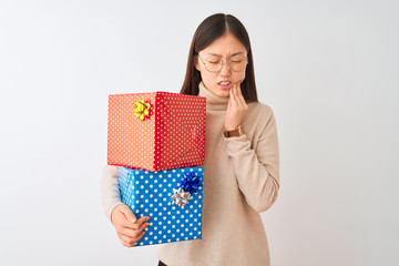Young chinese woman holding birthday gifts over isolated white background touching mouth with hand with painful expression because of toothache or dental illness on teeth. Dentist concept.