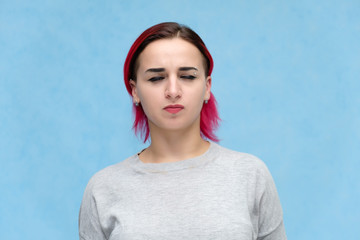 Portrait of the chest of a pretty girl with red hair on a blue background in a gray jacket. Standing in the studio right in front of the camera with emotions, talking, showing hands, smiling